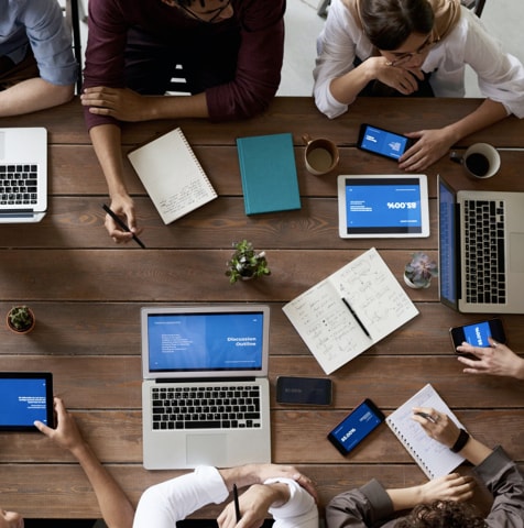 overhead shot of people gathered around table with computers and notepads