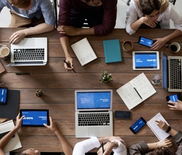 overhead shot of people gathered around table with computers and notepads