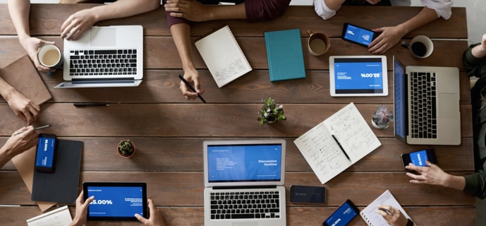 overhead shot of people gathered around table with computers and notepads